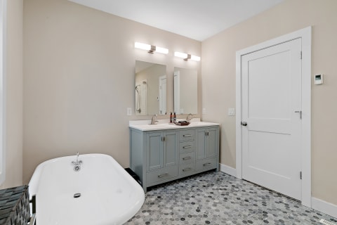 Modern bathroom with gray vanity, mirrors, and freestanding bathtub.