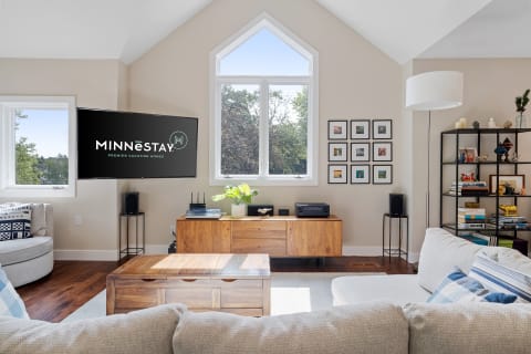 Modern living room with wooden furniture, a TV displaying 'MINNESTAY', and framed pictures on the wall.