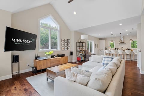 A bright living room featuring a flat-screen TV, comfortable sofa, and a stylish kitchen in the background.