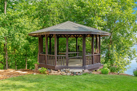Wooden gazebo in a green setting with a view of the water.