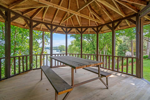Wooden gazebo with a table and benches, looking out over a lake surrounded by trees.