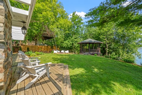 Outdoor seating area with white chairs, gazebo, and green landscape next to a body of water.