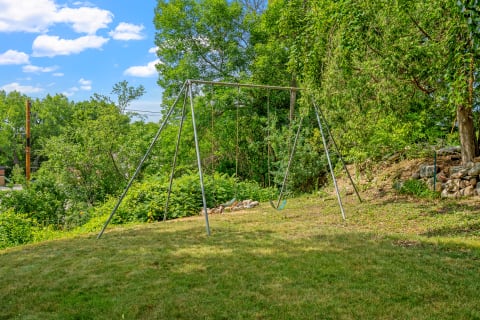A swing set in a green yard under a blue sky with clouds.