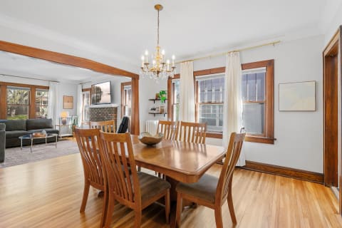 Dining area featuring a wooden table, chairs, chandelier, and a view into a living room with a sofa and fireplace.