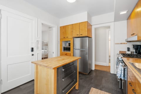 Interior view of a contemporary kitchen with an island, wooden cabinets, and stainless steel appliances.