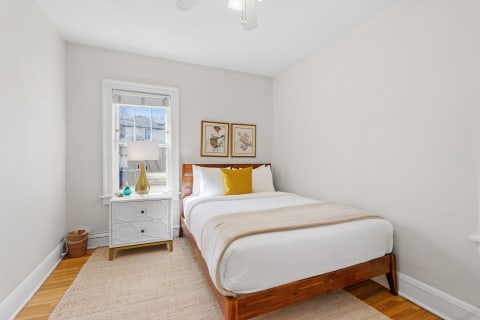 Cozy bedroom featuring a bed with white linens, a yellow pillow, and decorative wall art.