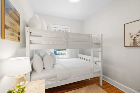A cozy bedroom featuring a white bunk bed, a bedside lamp, and a small decorated table.