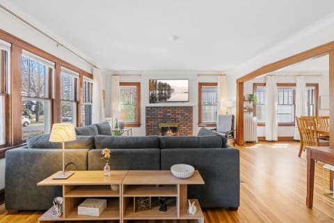 Cozy living room with a gray sectional sofa, a brick fireplace, and large windows.