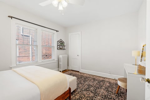 Bright bedroom with a cozy atmosphere, featuring a bed, working desk, and natural light from windows.