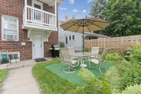 Outdoor patio area with table and chairs near a brick wall and greenery.