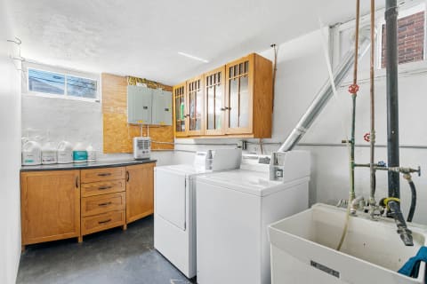 Bright basement laundry room featuring washing machines, a countertop, and storage cabinets.