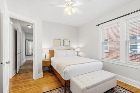 A bright bedroom featuring a king-sized bed, wooden flooring, and soft lighting.