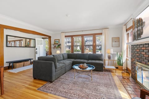 A spacious living room featuring a gray sectional sofa, large windows, and a warm ambiance.