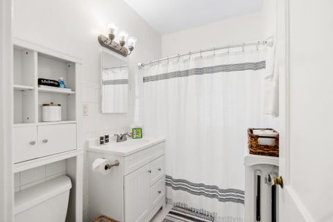 A clean and modern bathroom featuring a white color scheme, a shower with a striped curtain, and organized storage.