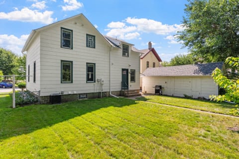 Two-story white house with green windows and a backyard in sunlight.
