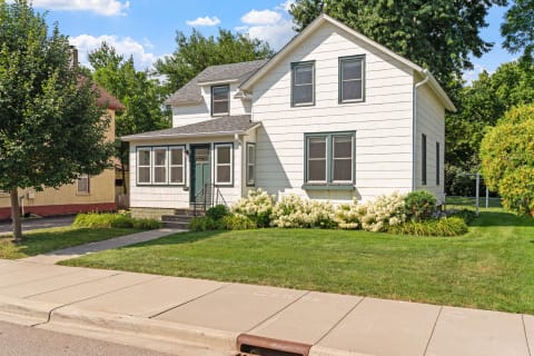 Two-story white house with green trim and flowering plants in the front yard.