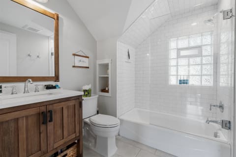Modern bathroom with white tiles, a wooden vanity, and a glass block window.