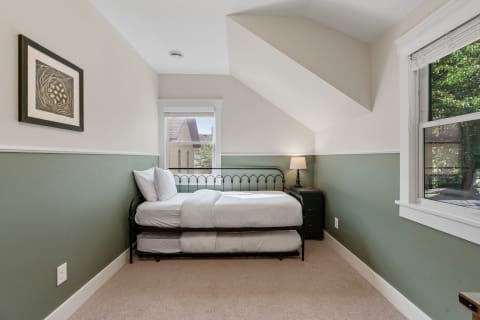 A neatly arranged bedroom with a single bed, green wall, and a window.