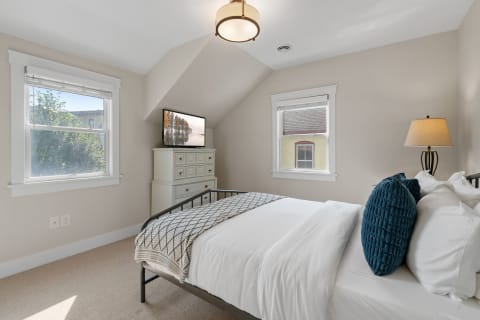 A cozy bedroom featuring sloped ceilings, a neatly made bed, and natural sunlight.