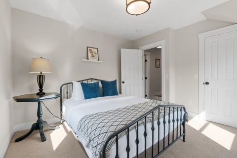 A cozy bedroom featuring a bed with blue pillows, a side table with a lamp, and soft lighting.