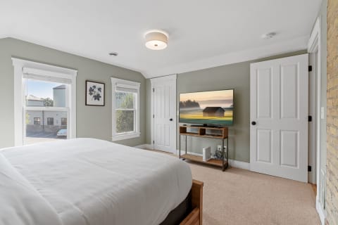 Cozy bedroom with a bed, window, and wall-mounted TV displaying a serene landscape.