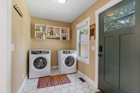 Laundry room with white washing machines, wooden shelf, and a green door.