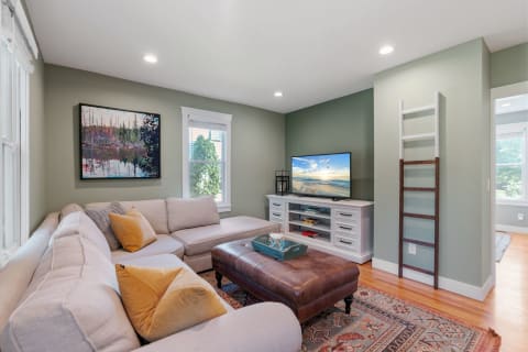 A light-filled living room featuring a sectional sofa, TV, and landscape painting.
