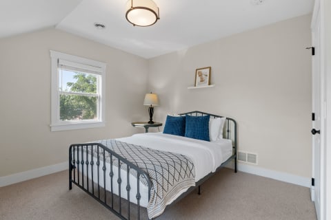 Cozy bedroom featuring a metal bed frame, blue pillows, and natural light from a window.