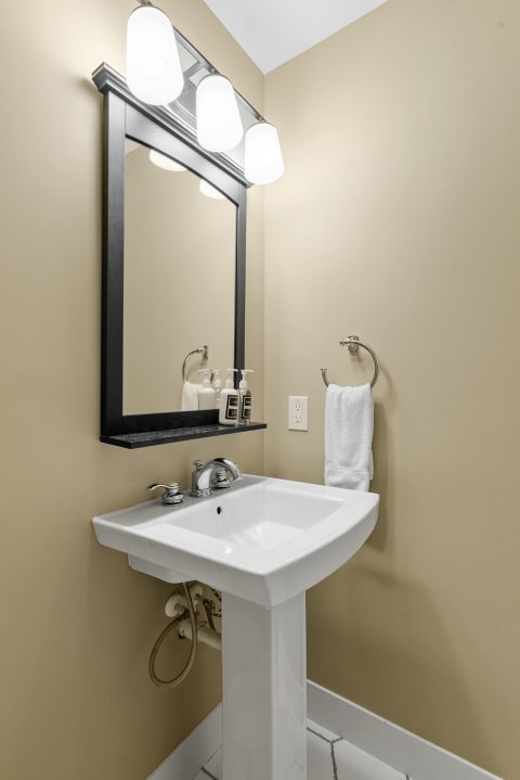 A clean and modern bathroom with a white pedestal sink, black-framed mirror, and soft lighting.
