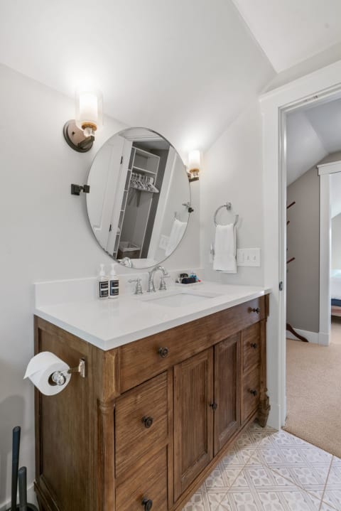 View of a modern bathroom featuring a wooden vanity, round mirror, and patterned tiles.