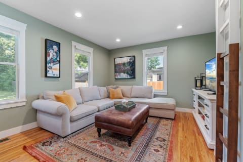 A cozy living room featuring a sectional sofa, an ottoman, and large windows with natural light.