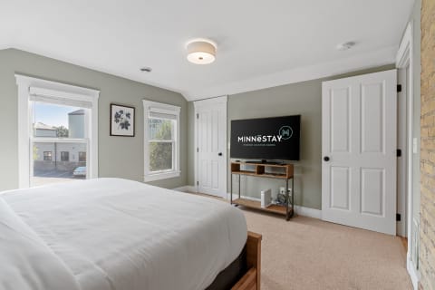 Cozy bedroom with white bed, TV, and natural light.