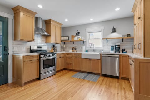A modern kitchen with light wood cabinets, stainless steel appliances, and a farmhouse sink.