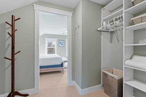 Entryway with a coat rack, shelving, and a glimpse of a cozy bedroom in the background.