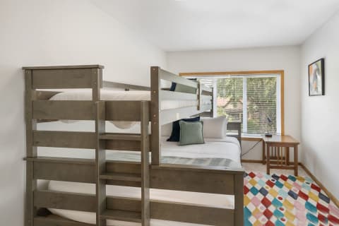 Cozy bedroom with wooden bunk bed, colorful rug, and natural light from a window.