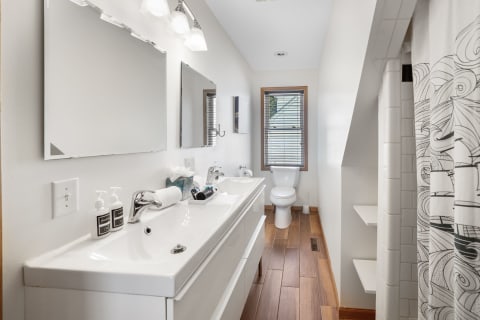 A sleek bathroom showcasing a double sink vanity, mirrors, and wooden flooring.