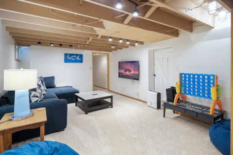 A comfortable basement living room featuring a sectional sofa, coffee table, and connect-four game.