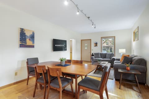 Cozy interior of a dining and living area with a wooden table, gray seating, and natural light.