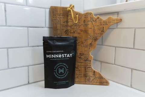 A coffee bag from MINNESTAY sits in front of a wooden map of Minnesota against white tiles.