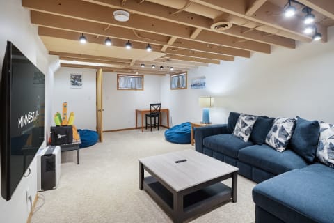A cozy basement living area featuring a navy sectional sofa, coffee table, and bright lighting.
