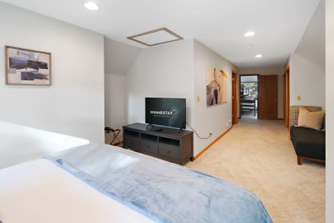 A spacious modern room with a bed, TV unit, and hallway, decorated with abstract art.