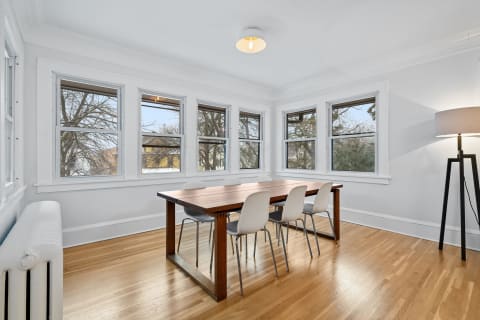 Bright dining room with wooden table and white chairs, featuring large windows.