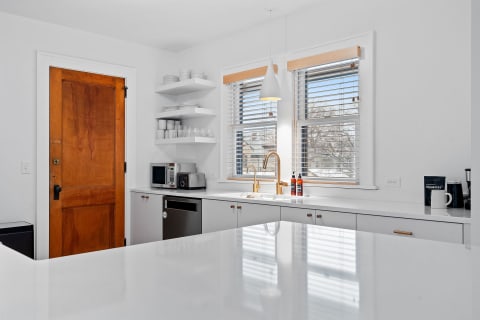 A contemporary kitchen with white cabinets, a wooden door, and a modern pendant light.