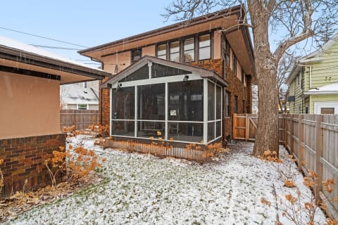 A two-story house with a screened-in porch in winter, surrounded by snow and a wooden fence.