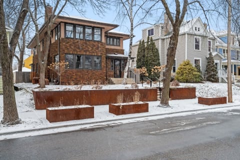 A two-story brick house in winter with rust-colored planters and snow-covered ground.
