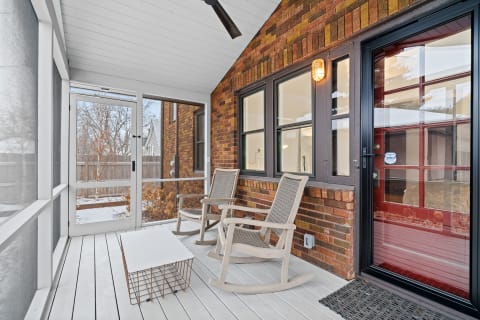 A spacious enclosed porch with two rocking chairs and a striking red door.