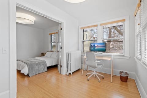 A bright room with a bed and a desk setup, showcasing a workspace and sleeping area.