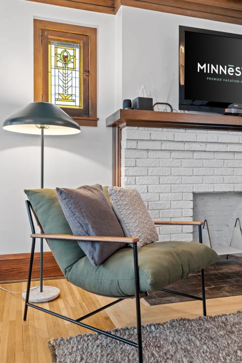 Cozy living room corner with a green armchair and decorative pillows, illuminated by a floor lamp.