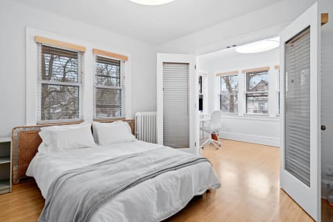 A bright bedroom featuring a bed and an adjacent workspace with a desk and chair.