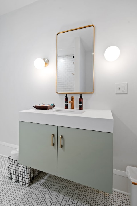 A contemporary bathroom vanity featuring a white countertop, green cabinet doors, and gold accents.